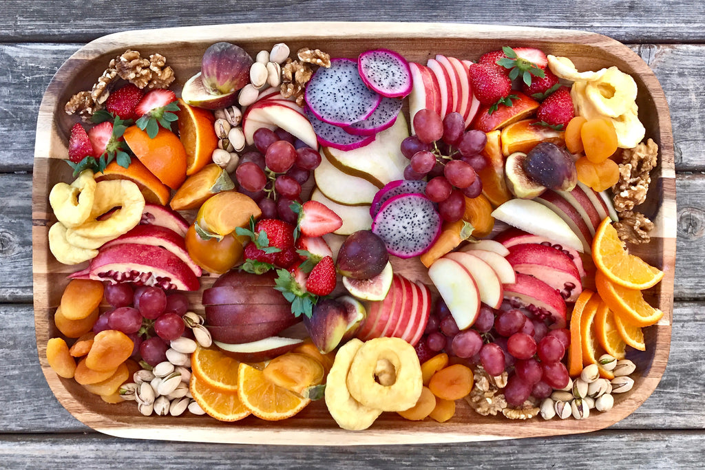 a bird's eye view of a large platter of cut fruits sits on a picnic table