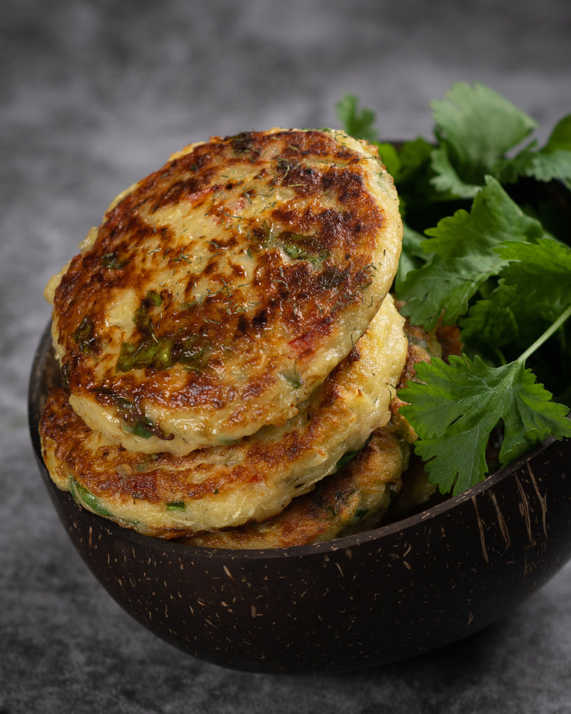 Image of a stack of vegetable fritters in a bowl with cilantro on a dark backdrop