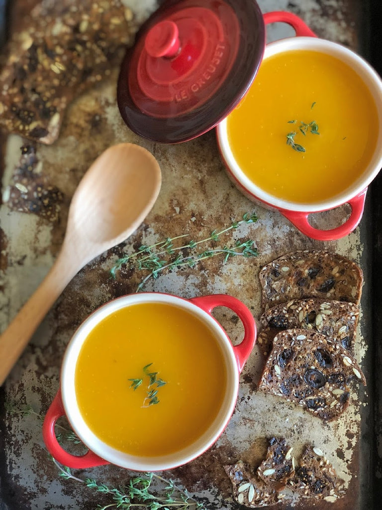 Small crocks of root veg soup sit on a baking sheet alongside toast, a wooden spoon and a sprig of thyme.